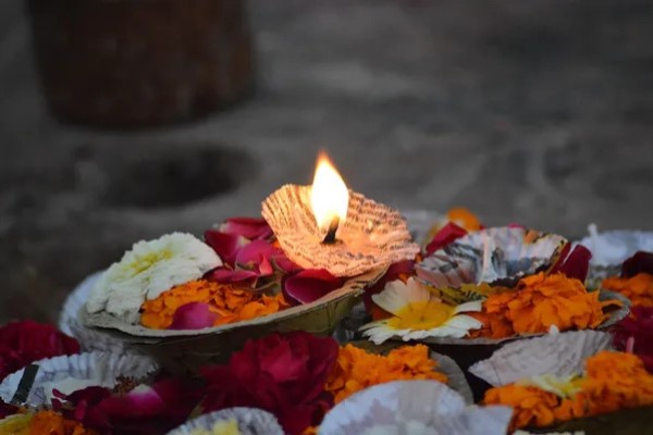 Small Tea Candle Lit Amongst Other Unlit Candles and Colorful Fall Flowers