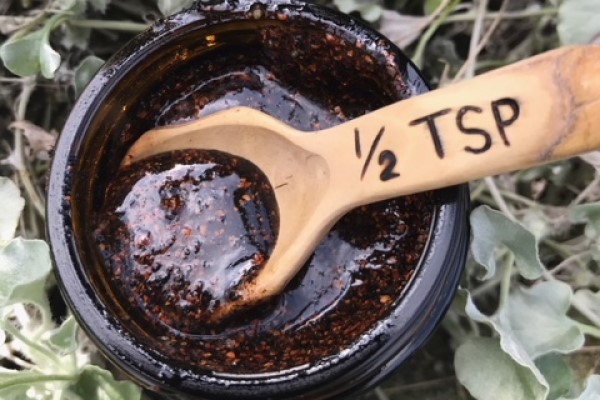 A wooden half teaspoon spoon in a jar of dark jam substance