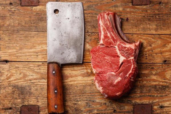 Meat cleaver next to a raw bone-in steak