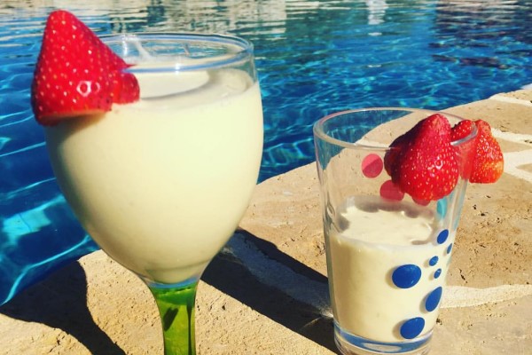 Two cups by the poolside filled with white smoothies, strawberries on the edges of the glass.