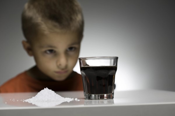 A young boy staring at a glass filled with dark liquid next to a pile of white powder