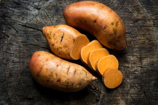 Three fresh sweet potatoes, one of which is chopped into slices