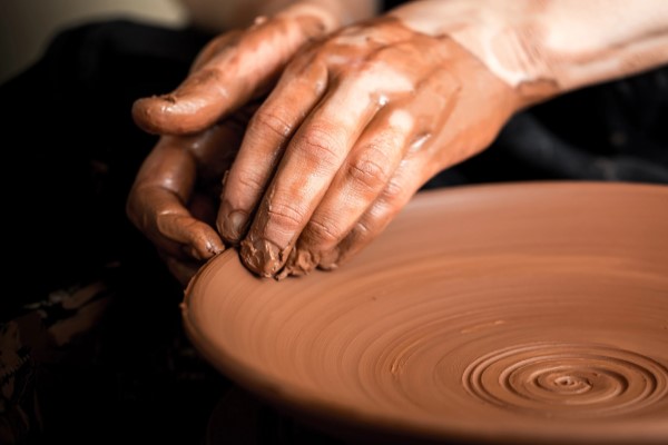 Two hands molding pottery clay on a spinning pottery wheel