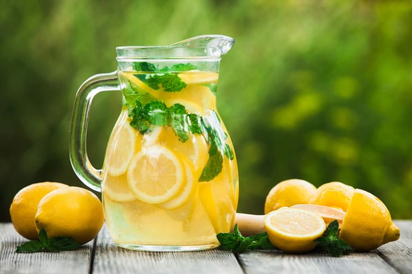 Clear pitcher of fresh lemonade surrounded by fresh cut lemons