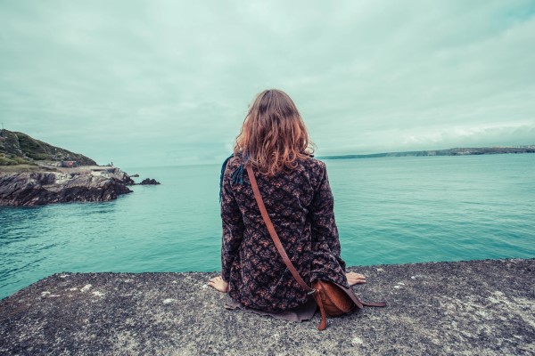 Woman sitting on the rocky shoreline, facing the horizon