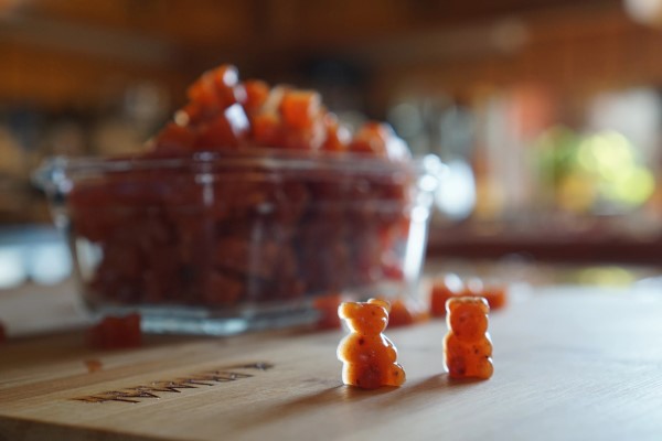 Glass dish filled with gummy bears; two gummy bears sitting upright on a cutting board