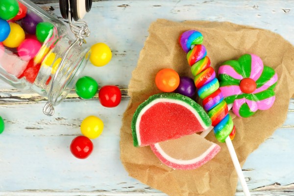 Colorful candy pieces and lollipops spilling out of a jar onto some parchment paper