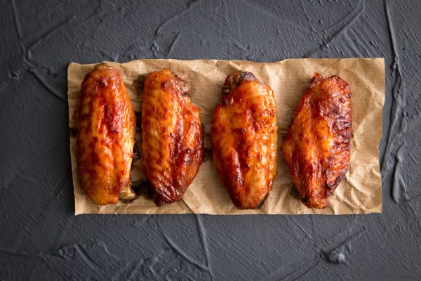 Four crispy, fried chicken wings lying on a brown paper towel